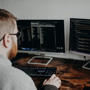 Developer writing code on two monitors at a wooden desk