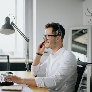 Man in an office talking on a phone headset at his computer
